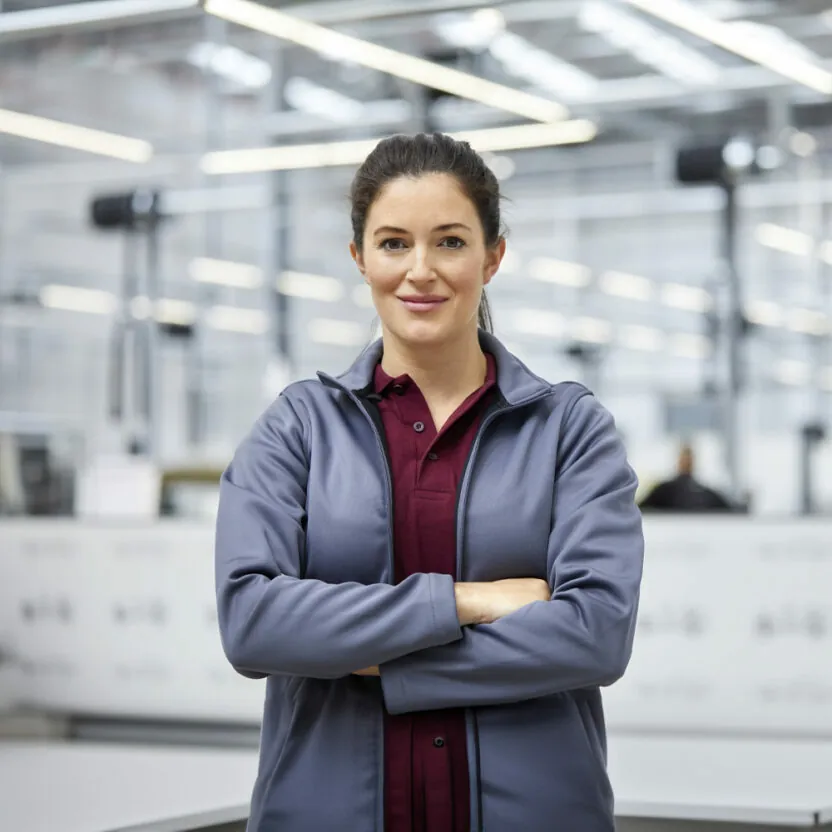 female-engineer-with-arms-crossed-in-car-plant-916868004 Portrait of female engineer with arms crossed in automobile industry. Confident technologist is standing in showroom. She is in jacket at factory.