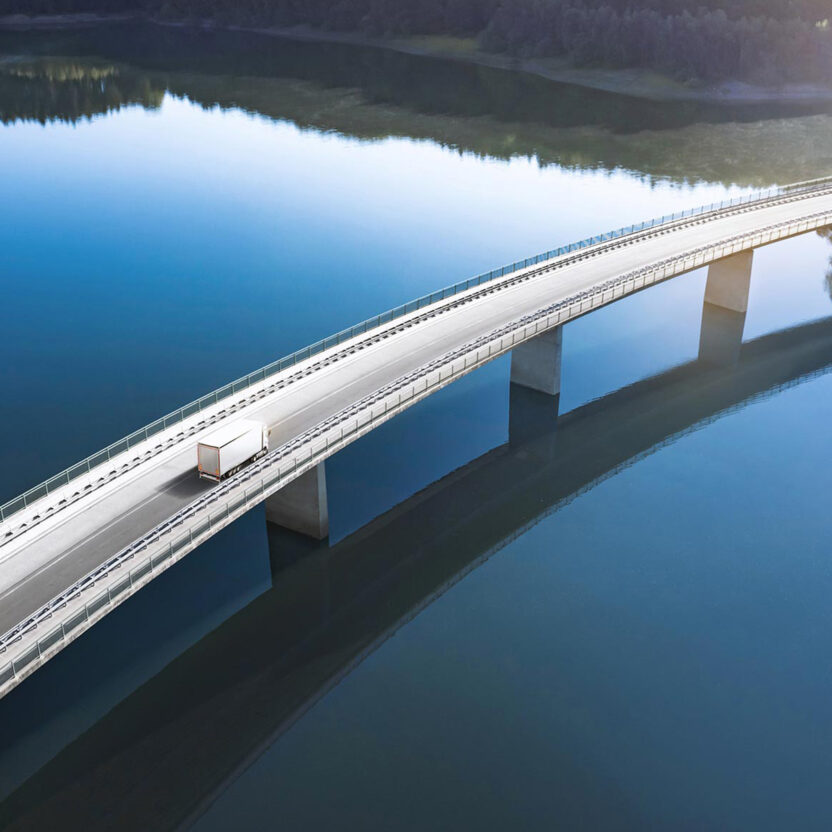 Die Eberspächer Gruppe schaltet durch die Zusammenarbeit mit valantic Austria einen Gang höher. Bild von einer großen Betonbrücke, die über strahlend blaues Wasser führt. Auf der Brücke fährt nur ein einzelner weißer Lkw. Am Rand kann man einen Wald erkennen.