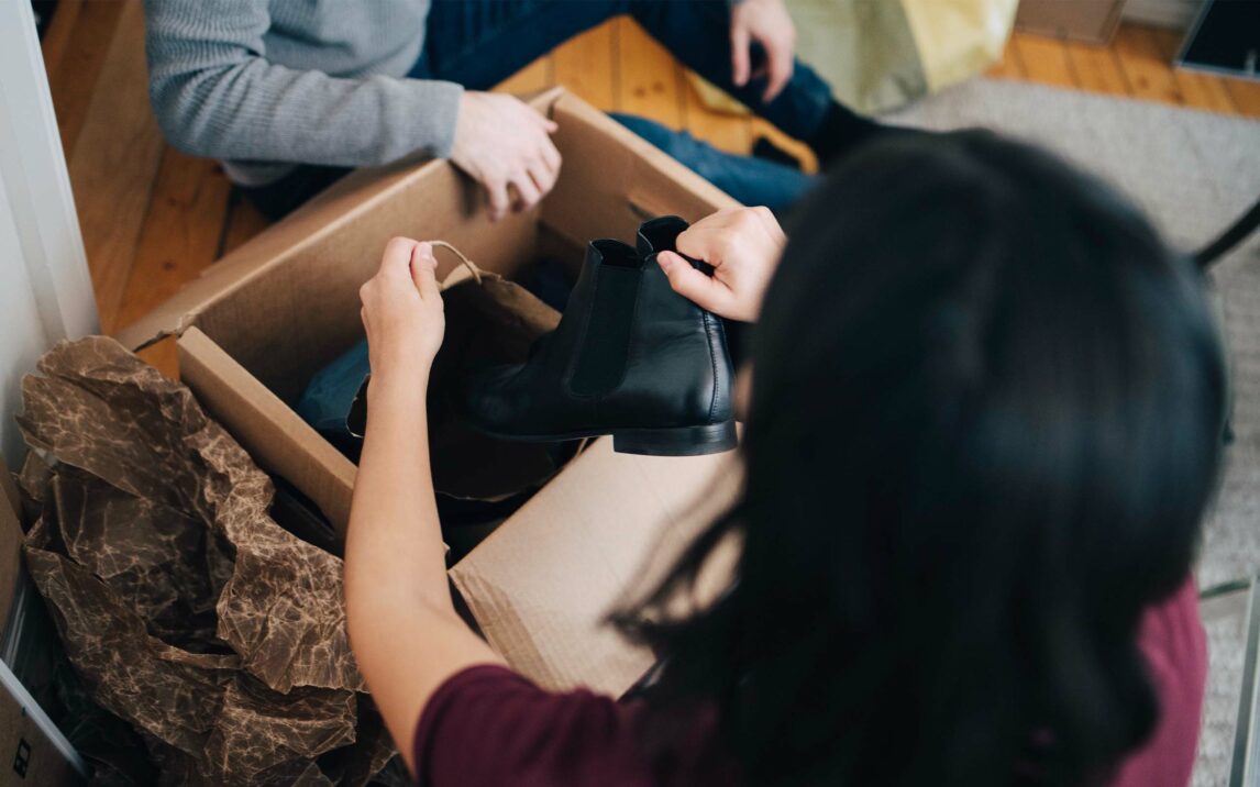 Woman removing shoe from box while sitting with man in apartment Woman removing shoe from box while sitting with man in apartment