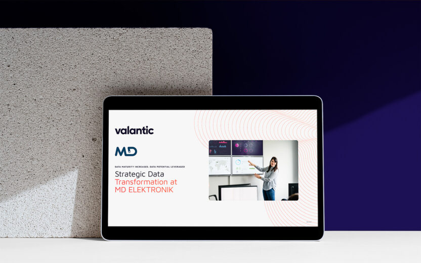 A tablet showcases a slide on strategic data transformation at MD ELEKTRONIK by valantic, highlighting data strategy. A woman gestures toward the screen adorned with insightful charts.