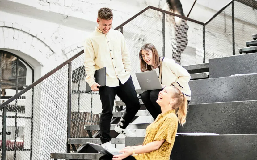 Photo of three colleagues sitting or standing on large steps, laughing.